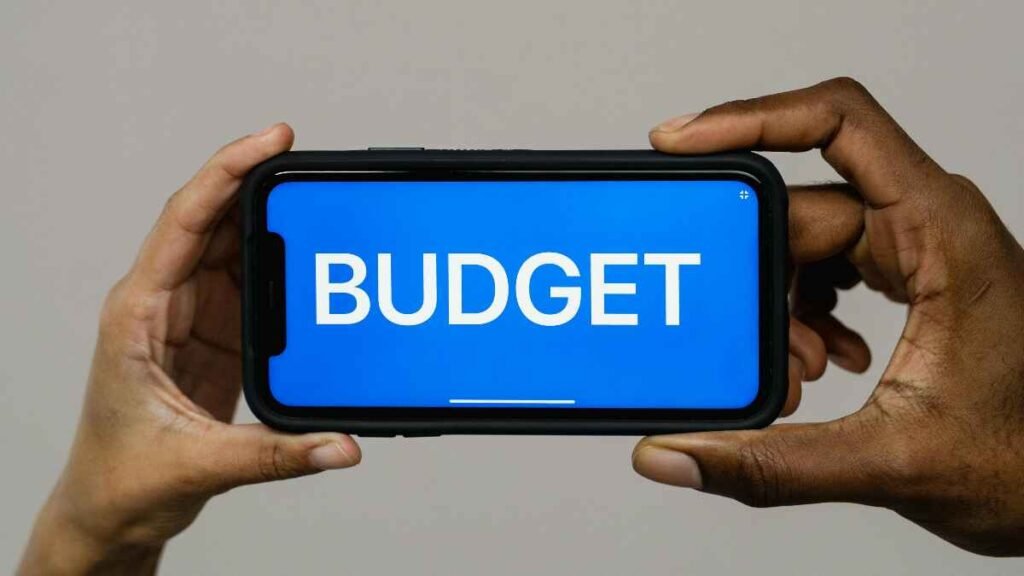 Hands holding a smartphone displaying the word BUDGET to represent budgeting apps and tools.