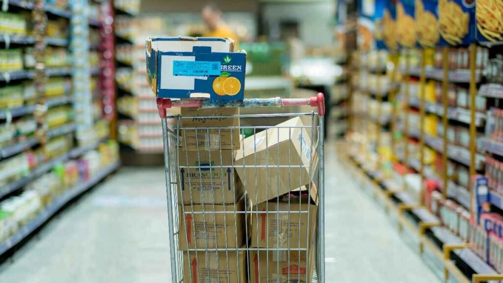 Shopping cart filled with boxes in a supermarket aisle showing how to cut grocery costs.