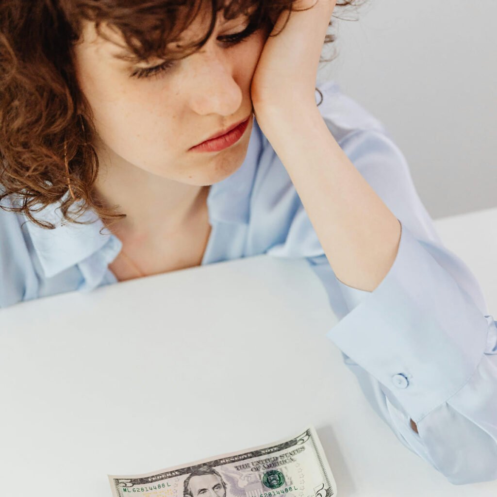 Sad woman looking at a five dollar bill struggling with financial stress and low income.